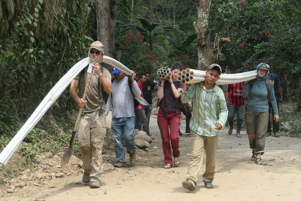 VAP students and community members working together to carry long, PVC pipes.