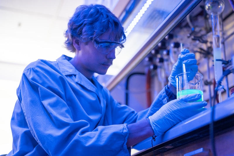 Student stirs a beaker under black light.