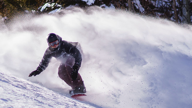 A snowboarder moving quickly over an alpine slope in a cloud of snow.